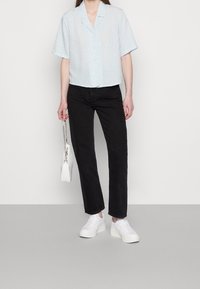Light blue short-sleeve button-up shirt with a subtle pattern, paired with black straight-leg jeans and white sneakers, holding a small white bag.