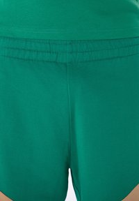 Πράσινο βαμβακερό σορτς με ελαστική μέση, διακοσμημένο με μια μικρή ταμπά λεπτομέρεια στο πλάι, με λεία υφή και casual σχεδιασμό.