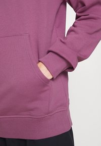 Bordeaux sweatshirt med ribbade mudd och nederkant. Har en ficka fram och mjuk textur, vilket betonar en avslappnad passform och casual design.