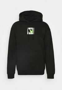Černá mikina s kapucí vyrobená z měkké látky, má přední kapsu a zelenou grafiku puzzle na bílém čtverci s textem "HUF".