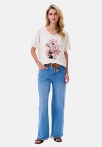 Losse crème katoenen t-shirt met bloemenprint, gecombineerd met blauwe hooggetailleerde denim jeans en zwarte platte sandalen met een eenvoudige band.