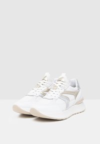 Sneaker bianche sportive con una parte superiore testurizzata, dettagli argentati, linguetta imbottita e una suola leggera e ammortizzata.