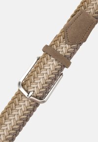 Flätad bälte i ljus beige och bruna toner, med ett metallspänne och en mockadetalj nära spännet, som visar upp textur och mönster.