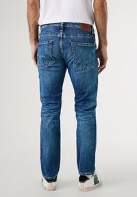 Blå denimjeans med en mid-rise passform, med bakfickor med unik sömnad och en brun läderlapp vid midjan.