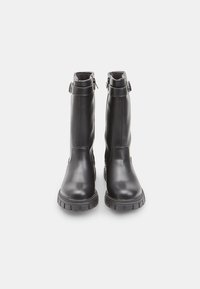 Černé kožené vysoké boty ke kolenům s kulatou špičkou, masivní gumovou podrážkou a bočními zipy. Obsahují akcenty na pásku poblíž vršku.