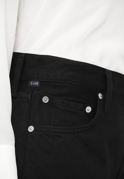 Melnas džinsa bikses ar teksturētu virsmu, sudraba aksesuāriem, nelielu uzrakstu "CofH" zīmi un klasisku piecu kabatu dizainu.