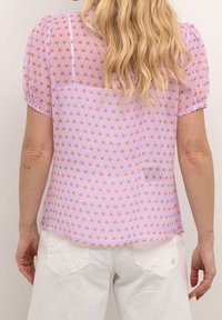 Top de manga corta en morado claro con un patrón de diamantes en naranja y blanco. Tejido suave y texturizado con un ajuste ligeramente holgado y dobladillo redondeado.