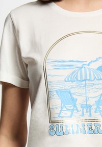 T-shirt in cotone bianco con una grafica di una scena da spiaggia blu, che mostra due sdraio, un ombrellone e la scritta 'ESTATE' con dettagli in blu e oro.