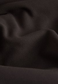 Tessuto nero con superficie liscia e leggermente testurizzata, che presenta pieghe e piegature delicate, indicando morbidezza e drappeggiabilità.