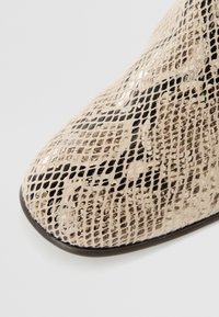 Beige snakeskin ankle boot with a textured pattern, pointed toe, and smooth black accents along the edges.