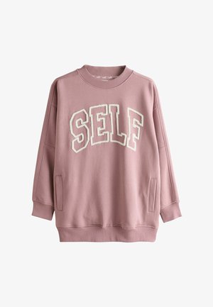 Hanorac roz cu inscripția „SELF” în litere pufoase albe. Prezintă un decolteu rotund, umeri căzuți și buzunare laterale. Textură moale a țesăturii.