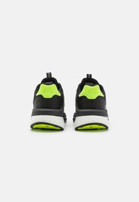Zapatillas de running negras con parte superior texturizada, acentos en el talón de color verde neón, entresuela blanca y suela exterior de goma negra con detalles verdes.