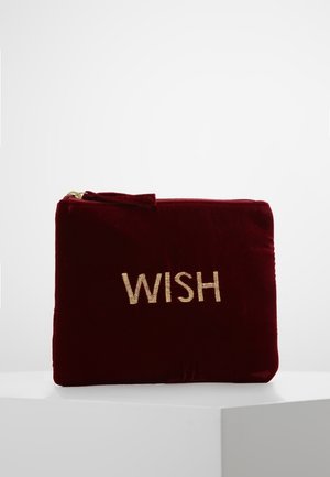 Tummanpunainen samettinen pussi, jossa on kultainen vetoketju ja edessä kultalangalla kirjailtu sana "WISH".