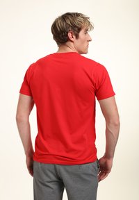Rød kortærmet t-shirt med rund hals, lavet af glat bomuldsstof. Båret med grå bukser, der viser et enkelt og rent design.