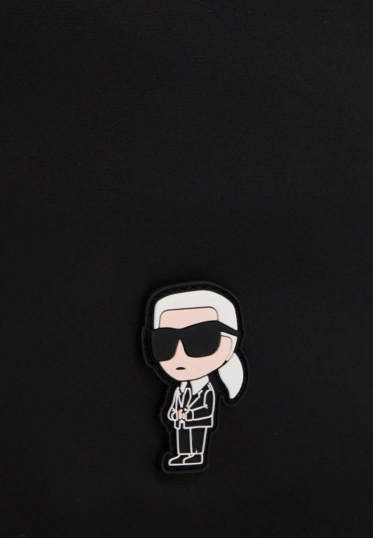 Personnage de dessin animé avec des cheveux blancs en queue de cheval, des lunettes de soleil noires, un costume noir et une cravate sur un fond texturé noir.