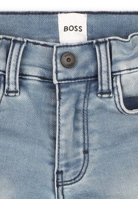 Jeans in denim blu chiaro con chiusura a bottone nera e etichetta del brand "BOSS" cucita sulla vita.