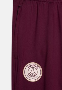 Bordeaux sportbroeken van gladde stof, voorzien van een zijzak en een ronde geborduurde logo met de tekst "PARIS" en "SAINT-GERMAIN".