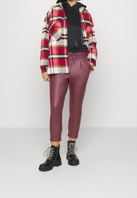 Rutig flanellskjorta i röd, svart och vit över en svart hoodie; högmidjade bordeauxfärgade byxor i konstläder; svarta snörboots.