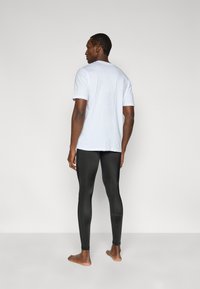 Λευκό T-shirt με διακριτικά μοτίβα στα μανίκια και μαύρο κολάν. Απλός σχεδιασμός, εφαρμοστό στυλ και λεία υφή.