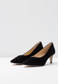 Chaussures à talons hauts en daim noir avec un bout pointu, un petit talon et un détail découpé à l'avant, offrant un intérieur lisse.