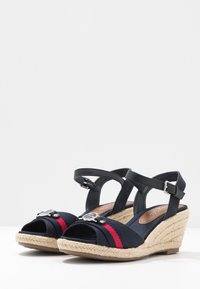Kloboučková sandály s horní částí z námořnické plátna, červeným pruhovaným zdobením, nastavitelnými černými kotníkovými popruhy a tkanou jutovou platformou.