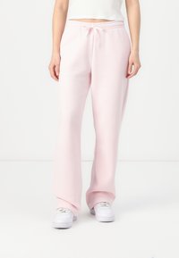 Pink sweatpants with an elastic waistband and drawstring. Made from soft fabric, featuring a loose fit and straight leg design. Worn with white sneakers.
