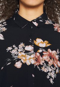 Černá květinová blůza s límcem, knoflíkovým zapínáním a kombinací růžových, oranžových a bílých květin se zelenými listy. Měkká textilie.