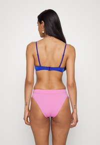 Két részes fürdőruha, amely egy kék melltartóból áll állítható pántokkal és egy rózsaszín bikinialsóból, sima anyaggal és letisztult dizájnnal.
