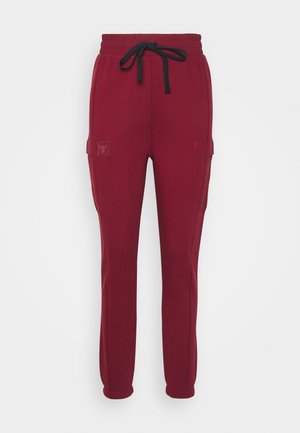 Burgundy jogger pants with elastic waistband, black drawstring, side pockets, and tapered legs against a white background.