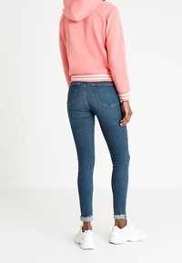 Sudadera rosa con rayas blancas, diseño cortado; combinada con jeans skinnies de mezclilla azul con dobladillo deshilachado y usados con zapatillas blancas.
