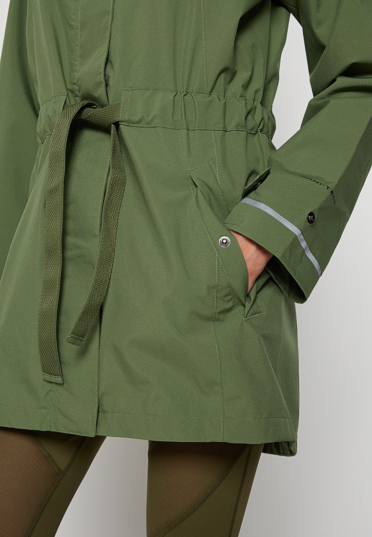 Zielona wodoodporna kurtka z regulowanym sznurkiem w talii, kieszeniami po bokach i odblaskowymi detalami na rękawach. Gładka faktura, nowoczesny design.