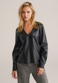 Schwarzes Kunstlederoberteil mit V-Ausschnitt, langen Ärmeln und einem eleganten Design. Glatte Textur mit einer mittigen Naht und figurschmeichelnder Silhouette.