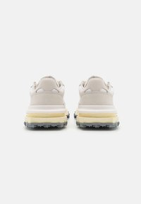 Chaussures de sport beige clair avec une tige en suède et en mesh, dotées d'une semelle épaisse jaune et grise avec des crampons texturés pour la traction.