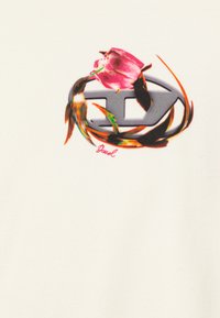 T-shirt graphique présentant un design floral coloré avec une rose rose entrelacée à un logo gris sur un fond en tissu crème.