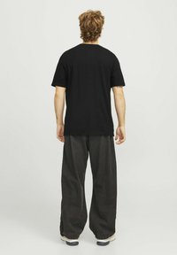 Sort bomulds T-shirt med en afslappet pasform, parret med løse, mørkegrå bukser. Bemærkelsesværdig tekstur og simpel design, velegnet til casual brug.