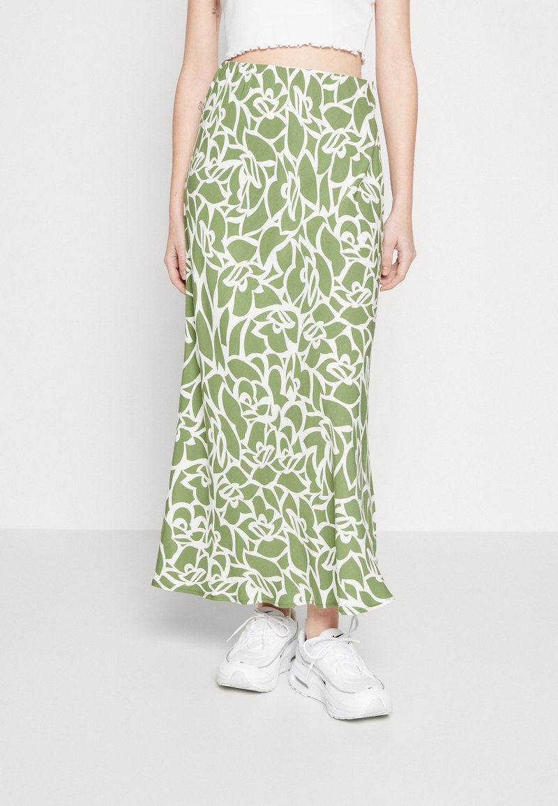 Falda maxi de tejido verde con un patrón floral blanco. Textura suave y diseño fluido, combinada con zapatillas blancas.