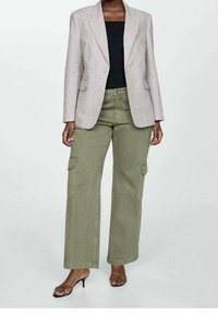 Blazer gris claro con un diseño estructurado sobre una blusa negra, combinado con pantalones cargo verde oliva. El look se completa con sandalias de tacón negras.