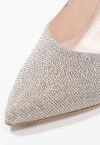 Szpilki o ostrym nosku w metalicznej srebrnej tkaninie, z teksturowanym wykończeniem i niskim wycięciem na cholewce dla smukłej sylwetki, z gładką skórzaną wkładką.