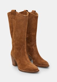 Botas de cowboy de ante marrón con detalles perforados, punta afilada y tacón de bloque medio. Incluyen una cremallera lateral para facilitar su uso.