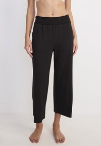 Zwarte, cropped wijde broek van zachte stof, met een brede elastische tailleband en twee voorzakken, met een gladde textuur.