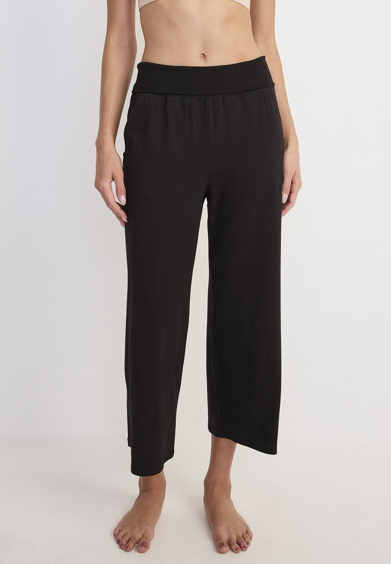 Zwarte, cropped wijde broek van zachte stof, met een brede elastische tailleband en twee voorzakken, met een gladde textuur.
