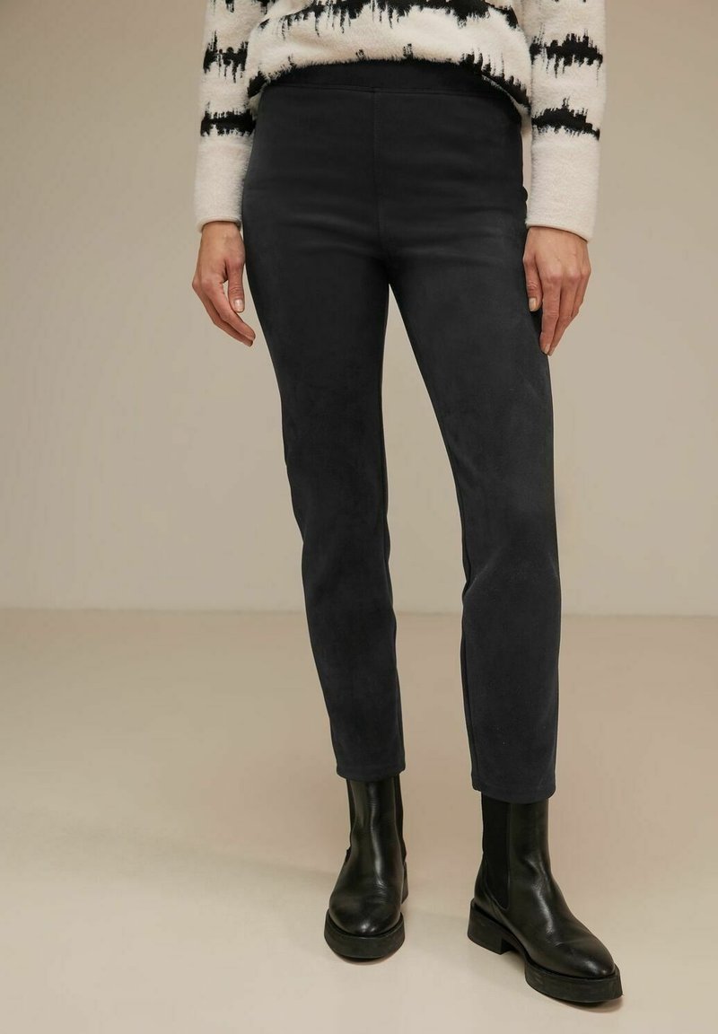 Black suede pants with a slim fit, featuring a smooth texture and ankle-length cut, paired with black ankle boots.