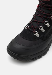 Black hiking boot featuring a textured upper, durable rubber sole, metal eyelets, and red-accented laces for secure fit and support.