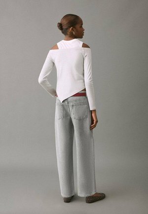 Hellgraues Langarmshirt mit ausgeschnittenen Schultern; kombiniert mit hoch taillierten, hellen Jeans und braunen Ballerinas mit Nietenbesatz.