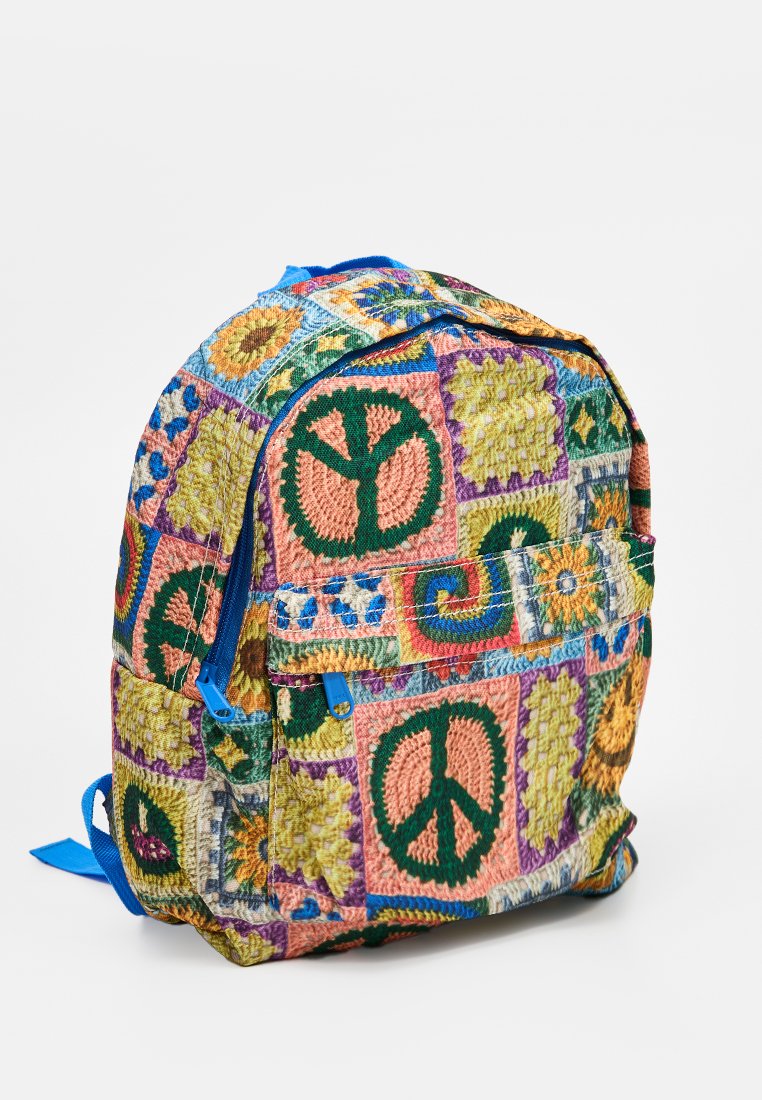 Sac à dos en tissu multicolore présentant des motifs de symbole de paix, des designs géométriques, une fermeture éclair bleue et des bretelles ajustables.