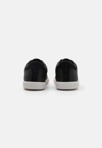 Zwarte sneakers met een gestructureerde leren en suède bovenkant, contrasterende witte rubberen zool en reliëfbranding op de hak.