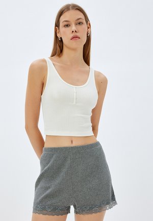Witte geribbelde crop top met een ronde halslijn en drie knopen. Gecombineerd met grijze geribbelde shorts met een kanten rand aan de onderkant.