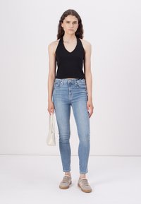 Crna halterCrop top, svijetloplave uske traperice, sivi tenisice i bijela torba. Model stoji uz jednostavnu pozadinu.