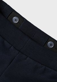 Ceinture élastique bleu marine avec texture côtelée, dotée d'une fermeture à bouton noir. Le tissu présente une finition lisse avec des détails de couture minimaux.