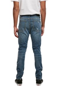 Modre kavbojke slim fit, s petimi žepi in postaranim videzom. Na hrbtu so šivi in klasičen pas.